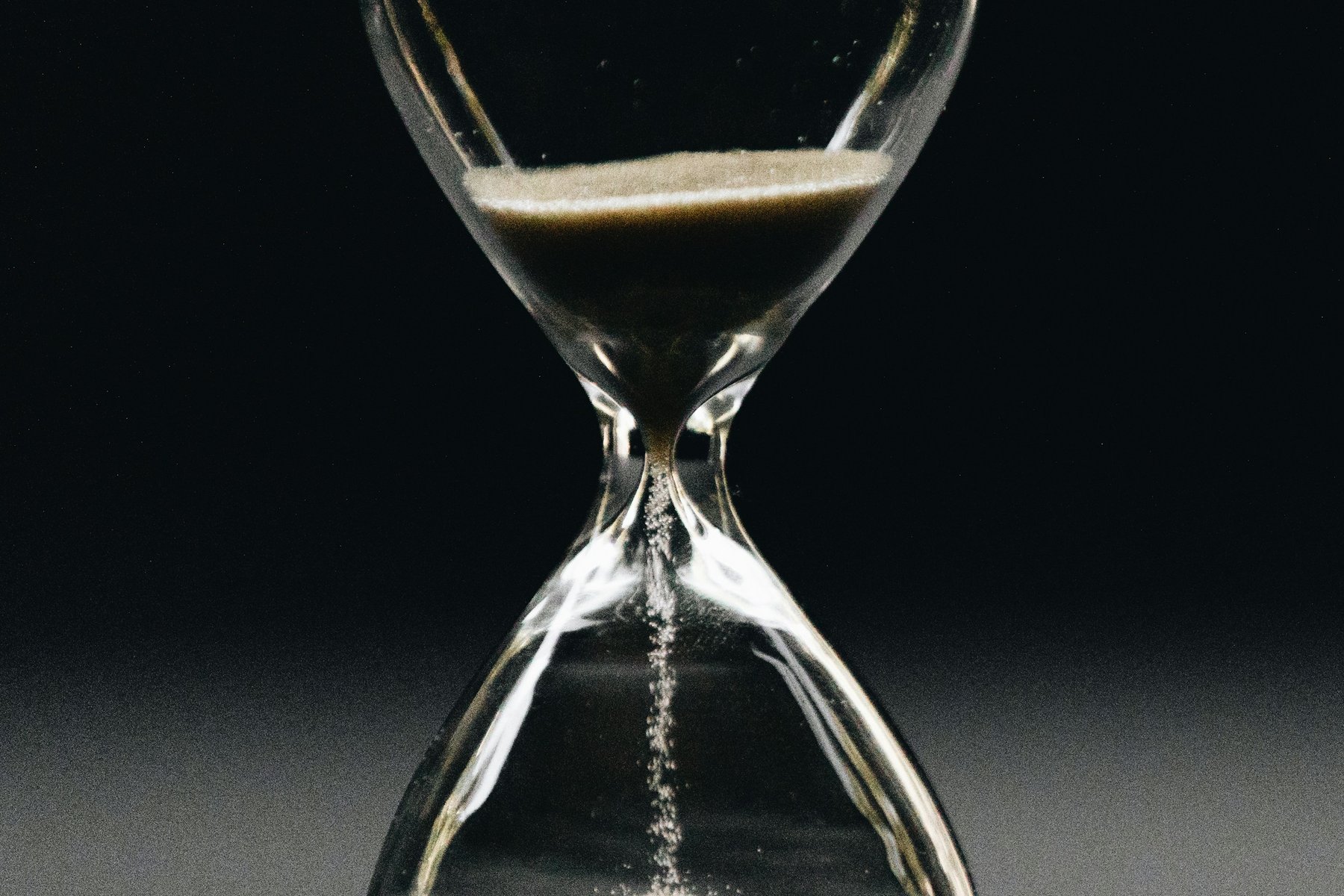 An hourglass with sand running through it, on a dark surface
