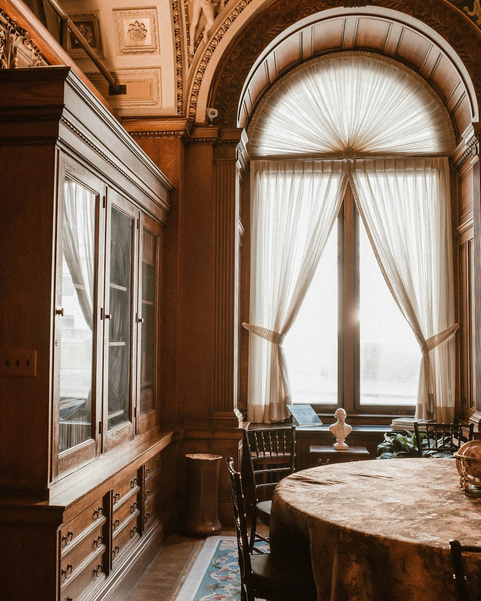 A wood-panelled room with an arched window and a round table