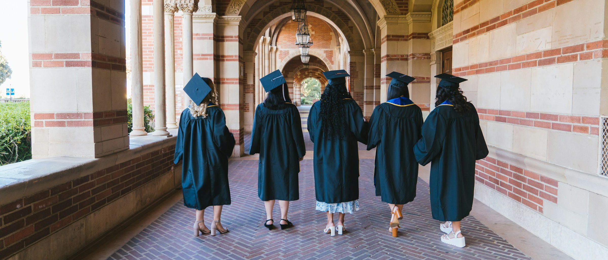 Graduates in gowns walking away along a sunlit university arcade