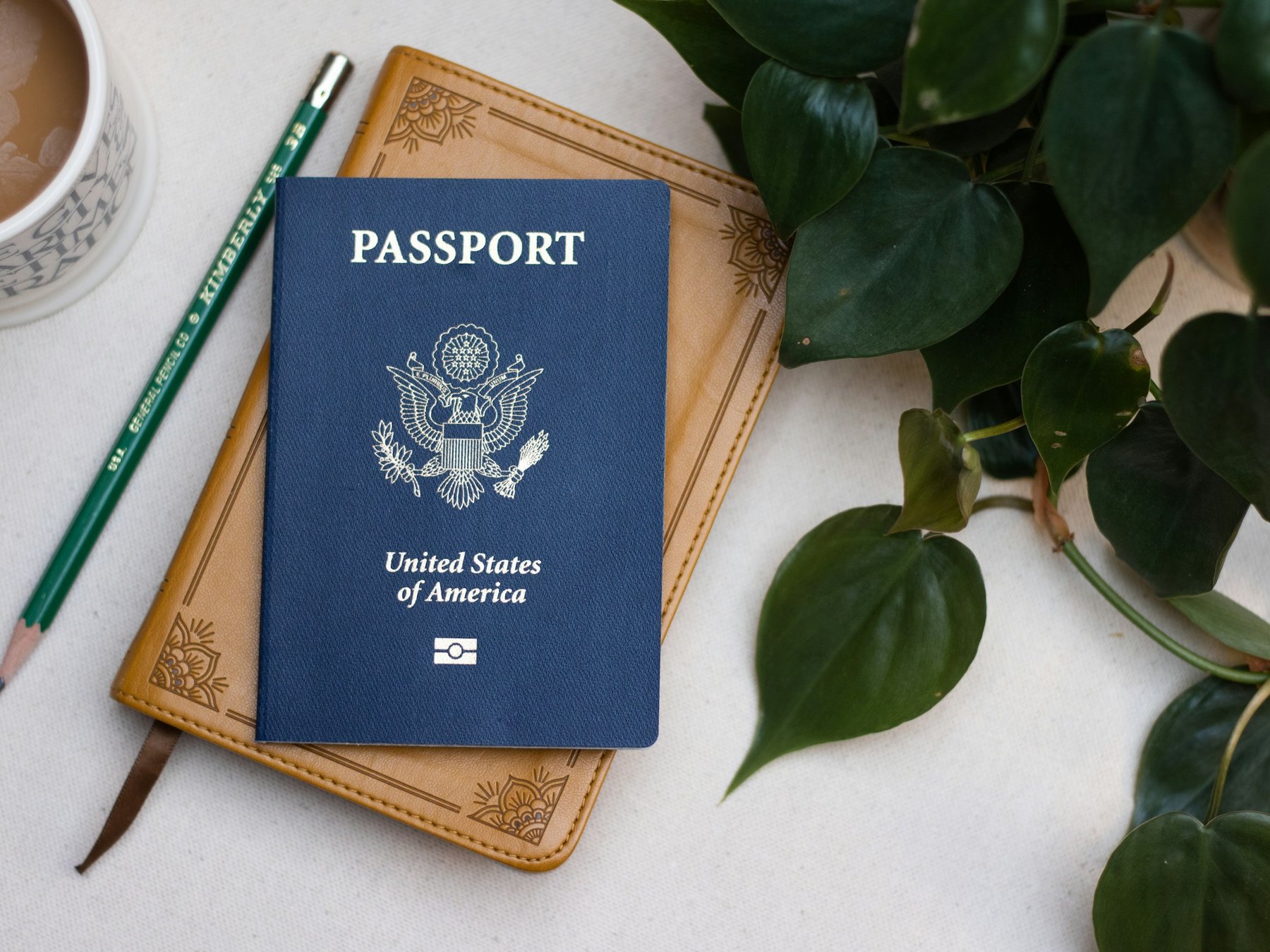 A United States passport on a desk beside a pencil, a notebook and a coffee